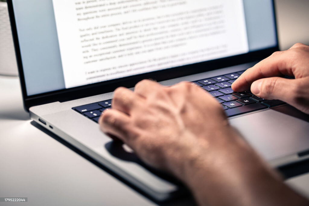 Close-up of a person's hands typing on a laptop keyboard with a document open on the screen.
